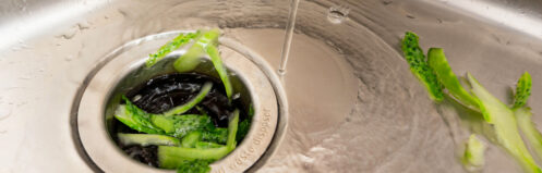 Garbage disposal handling cucumber peels with running water in a kitchen sink