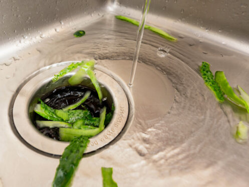 Garbage disposal handling cucumber peels with running water in a kitchen sink